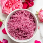 Bowl of pink rose sugar with fresh rose petals and blooms on marble