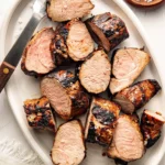 Grilled pork tenderloin sliced on a wooden board with charred edges