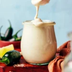 Creamy cheesy jalapeño cashew dressing being poured from a spoon into a jar
