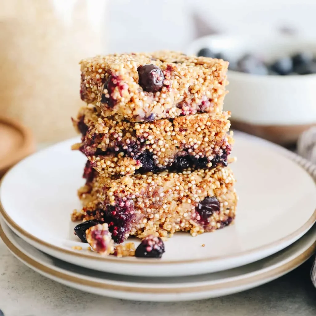 Stacked blueberry quinoa bars on plates with a bowl of fresh blueberries