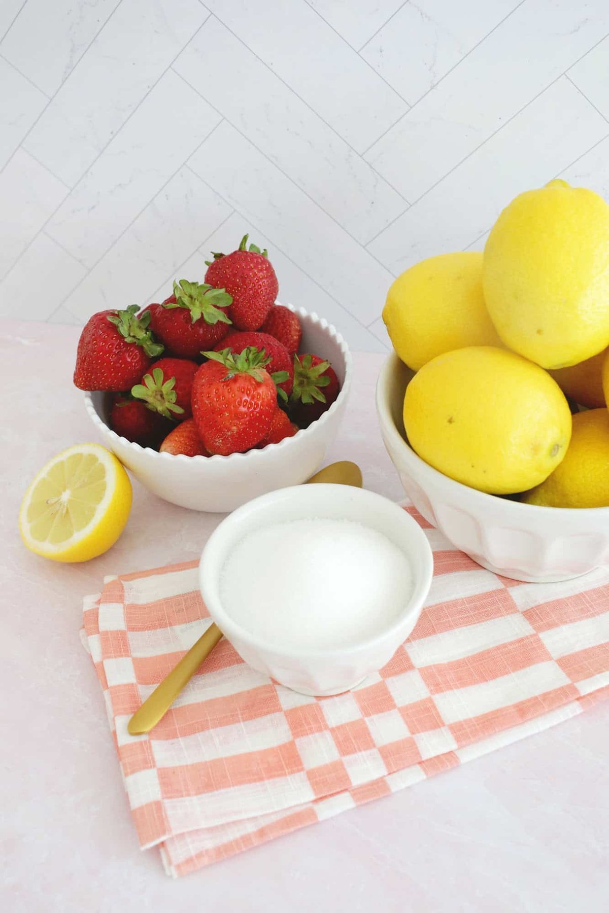 Bowls of fresh strawberries, lemons, and sugar on a checkered napkin