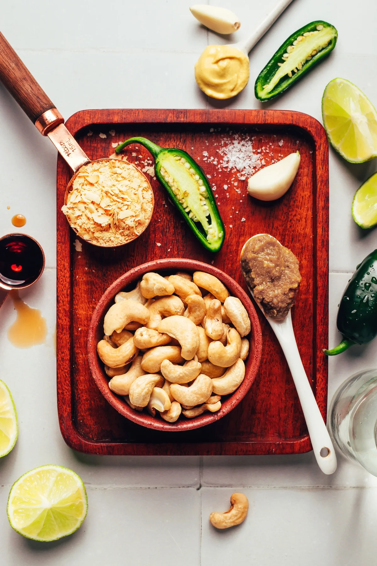Raw cashews, jalapeño, garlic, and lime arranged on a wooden tray