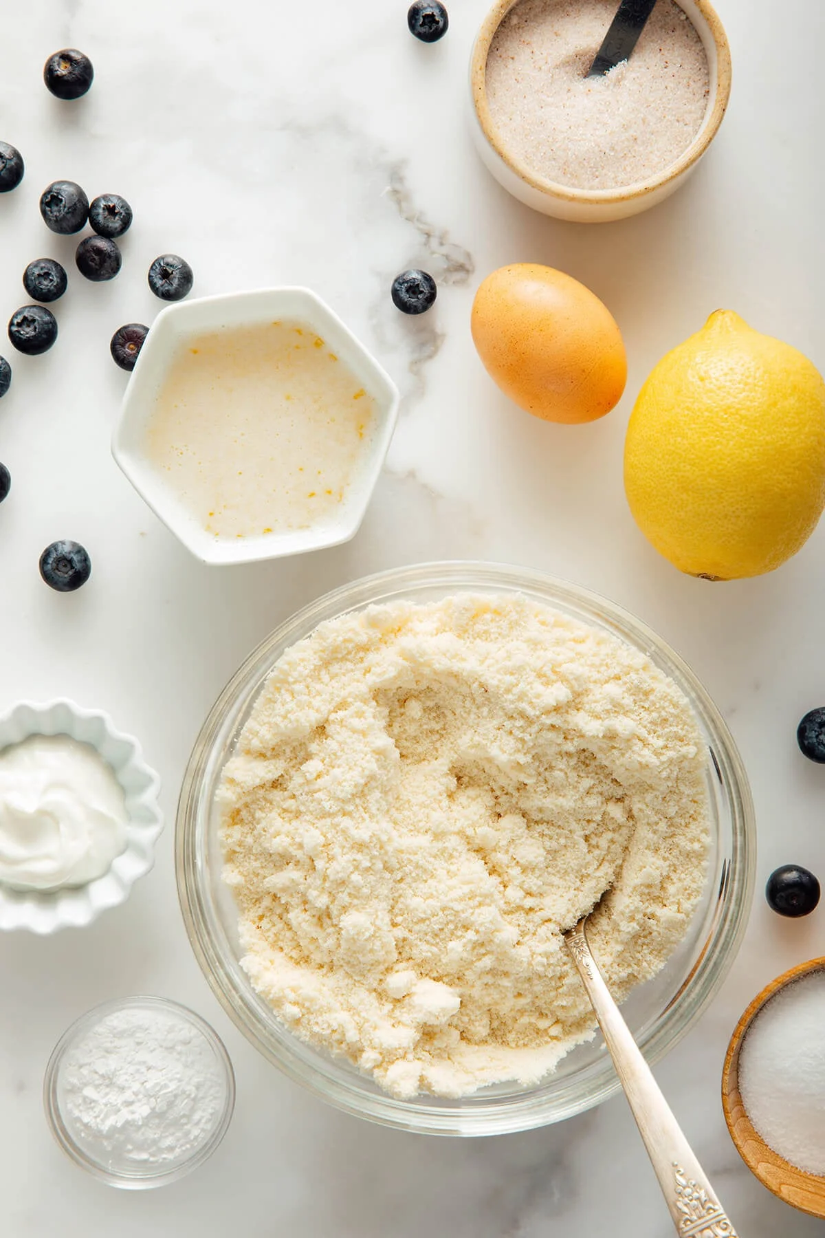 Almond flour, lemon zest, and blueberries arranged for baking