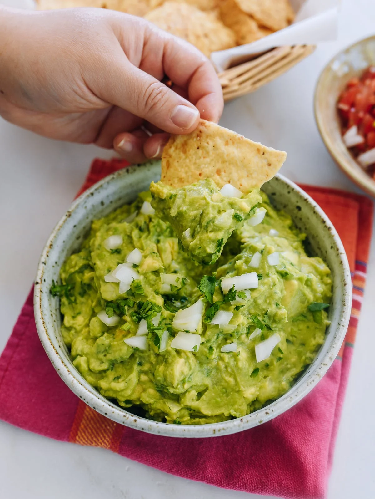 Tortilla chip dipped into a bowl of fresh chunky guacamole
