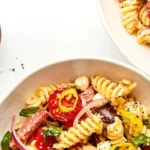 Bowl of Italian pasta salad with salami, tomatoes, and basil