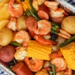 Aluminum tray piled with shrimp boil, corn, sausage and potatoes