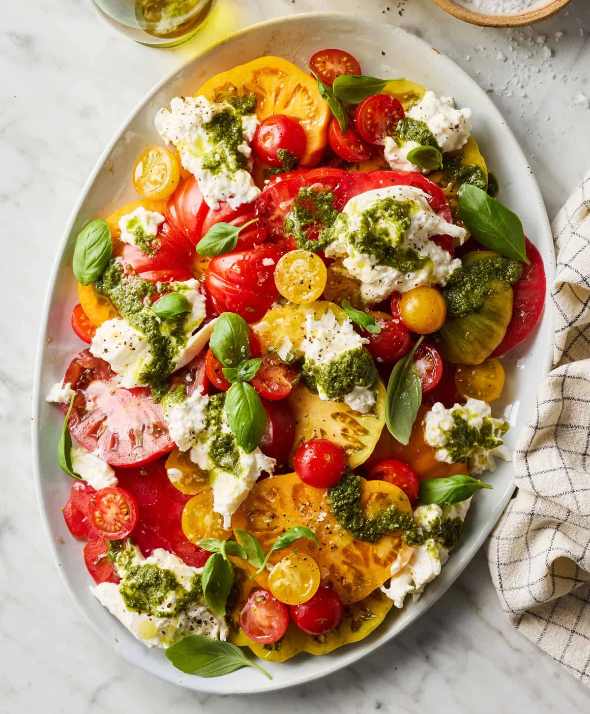Platter of sliced heirloom tomatoes, burrata, pesto, and basil