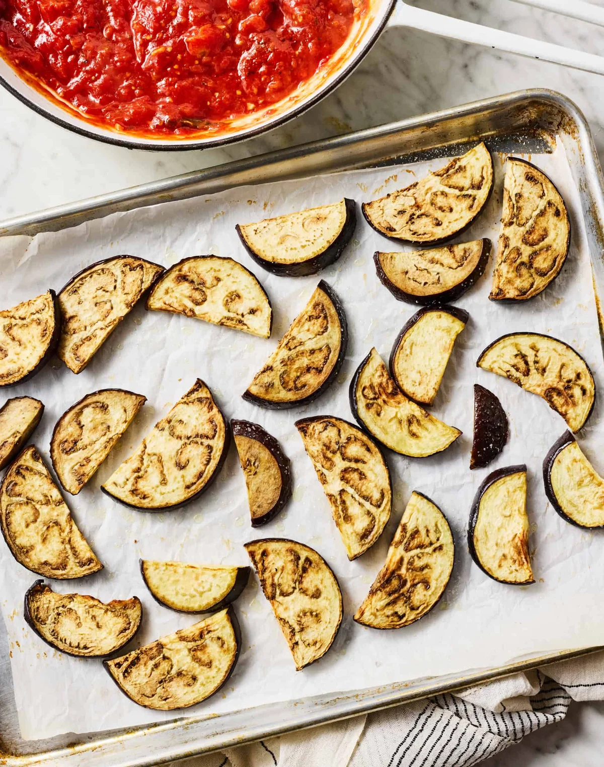 Roasted eggplant half-moons on parchment-lined baking sheets in the oven