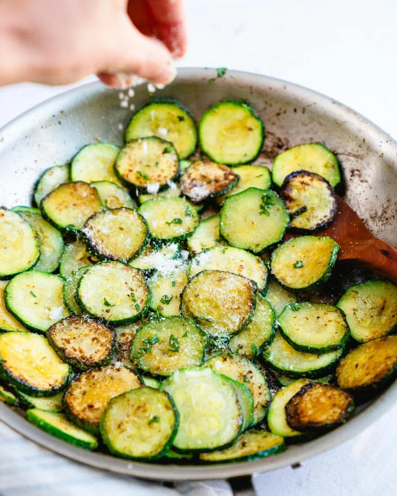 Zucchini rounds browning in a hot skillet with herbs