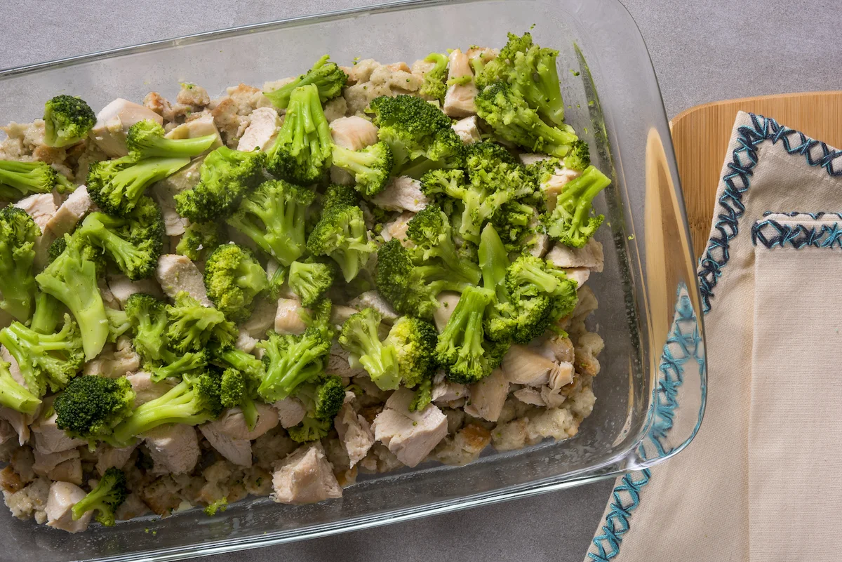 Broccoli florets and cubed chicken arranged over stuffing in a casserole dish