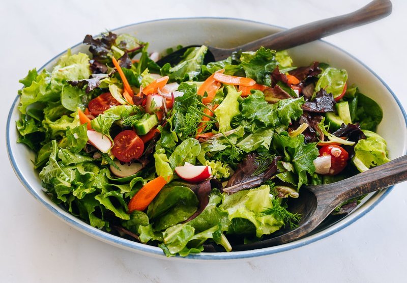 Green leaf salad with vegetables in a white ceramic bowl