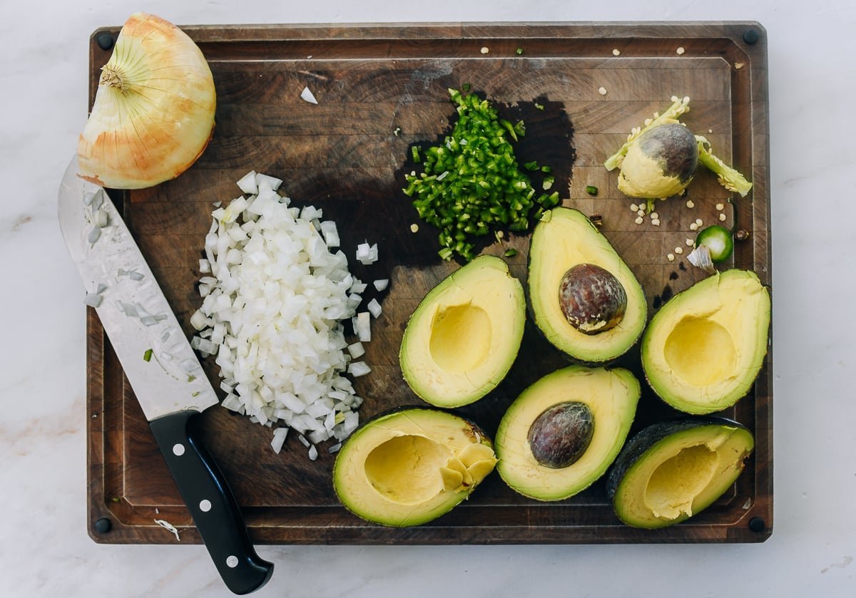 Cutting board with diced onion, minced jalapeño, and halved avocados