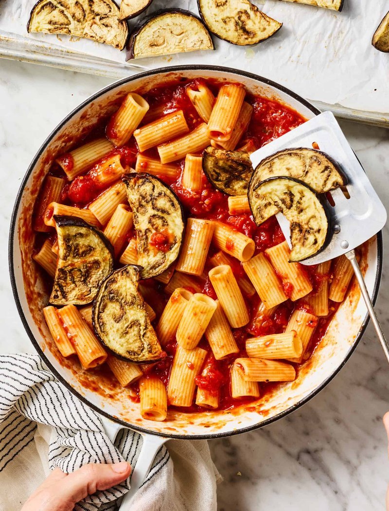 Rigatoni and roasted eggplant being tossed in tomato sauce in a pot