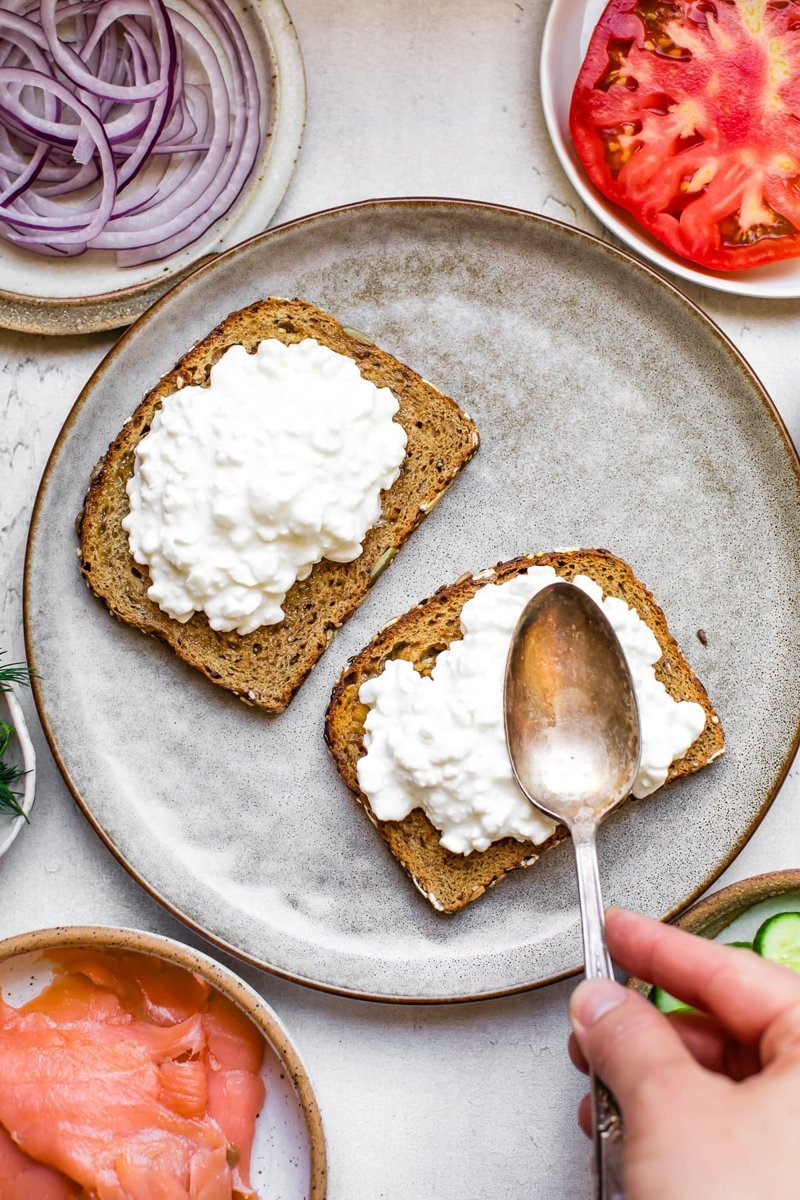 Assembling smoked salmon toast with toppings on whole-grain bread