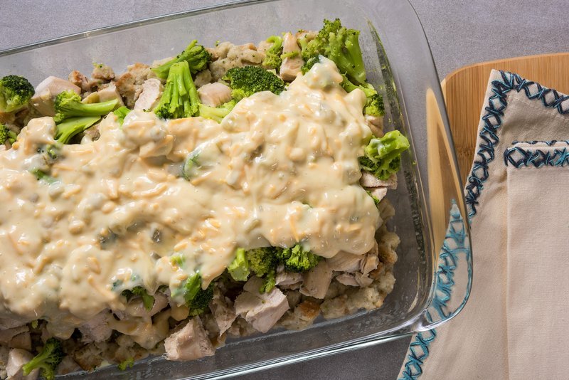 Chicken and broccoli casserole layered with sauce and cheese before baking