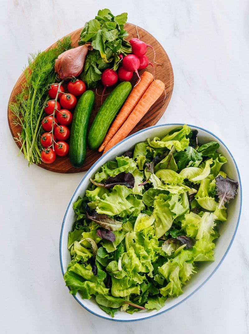 Cutting board with raw vegetables beside a bowl of mixed greens
