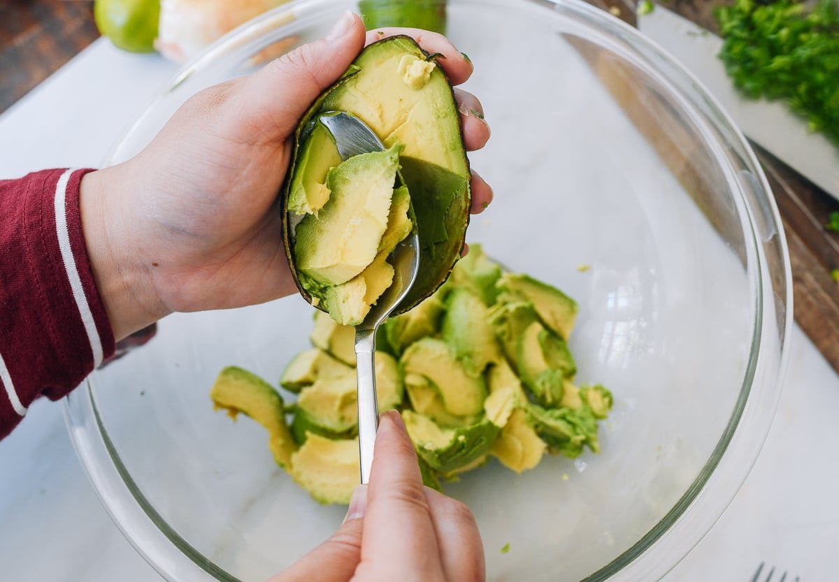 Scooping avocado chunks from a halved avocado into a glass bowl