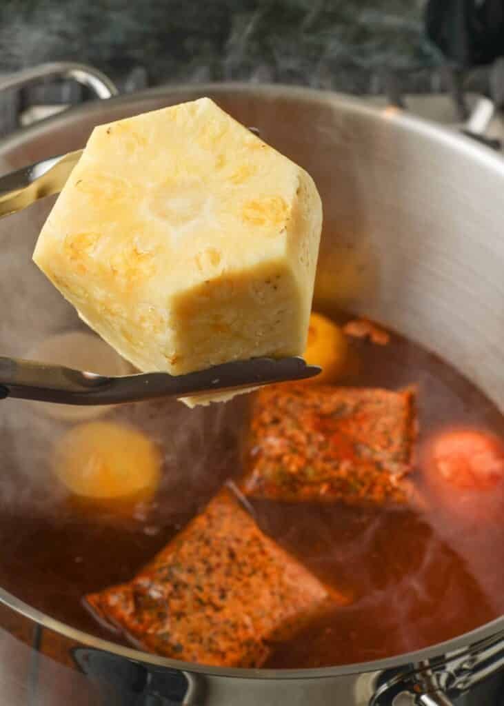 Whole cooked pineapple lifted from the spiced boiling broth