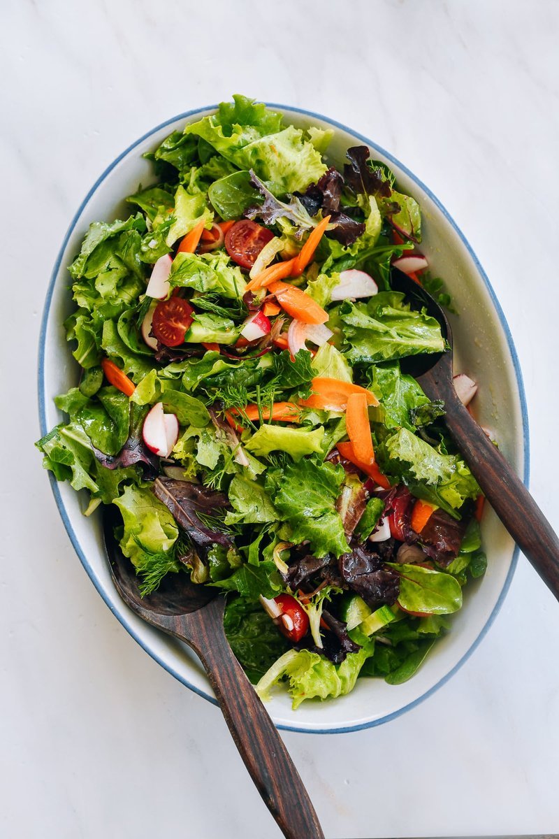 Finished side salad with wooden spoons in a white bowl