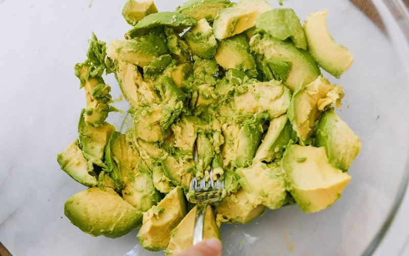 Fork mashing avocado with lime juice in a glass mixing bowl