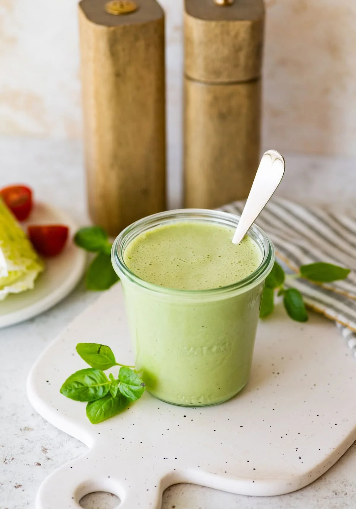 Green goddess dressing jar beside lettuce, tomatoes, and basil