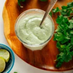 Jar of creamy cilantro lime sauce with limes and cilantro