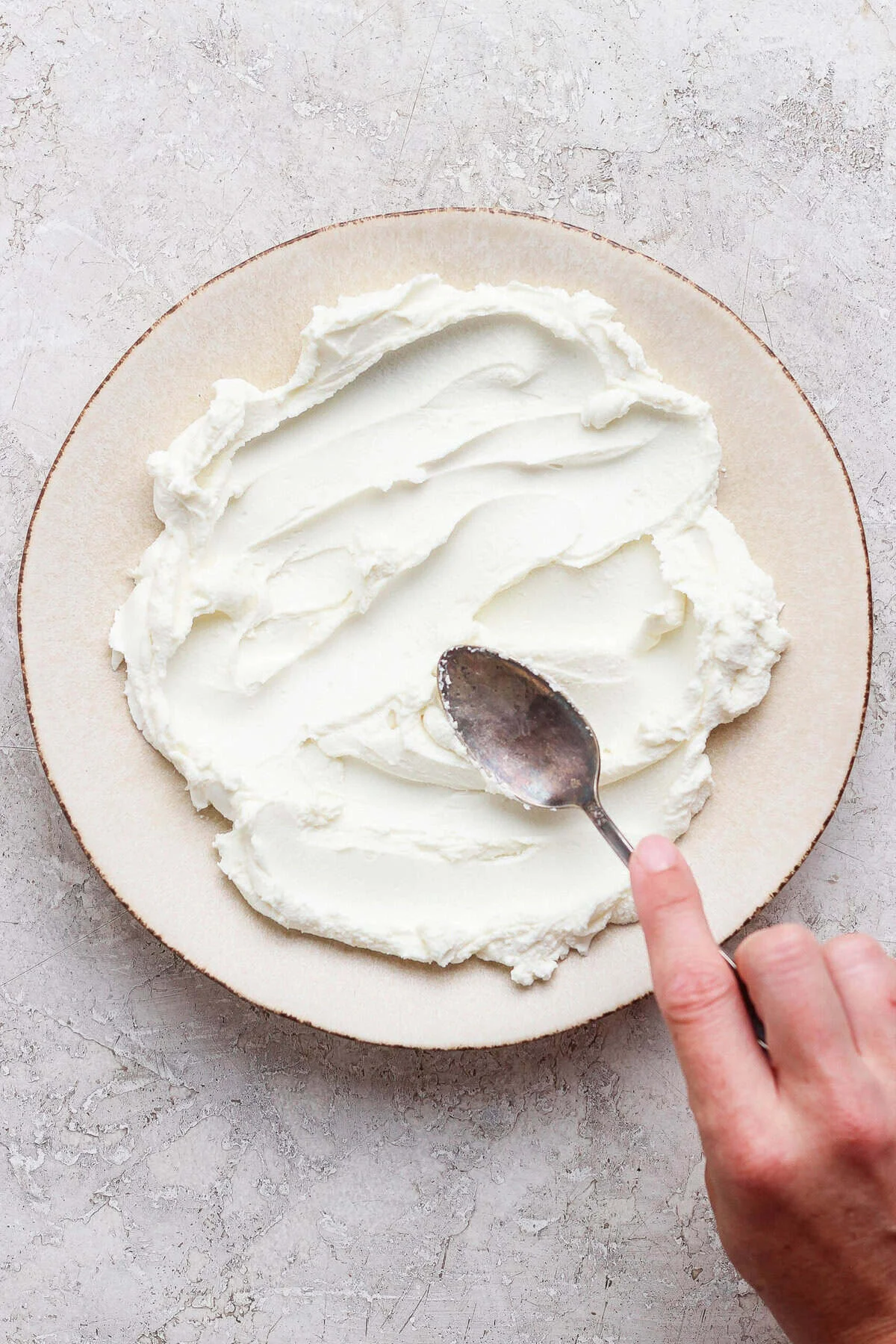 Softened goat cheese spread in swoops across a ceramic platter ready for toppings