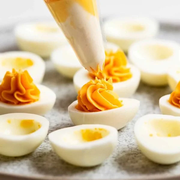 Deviled eggs being piped with a piping bag, orange filling on a neutral surface