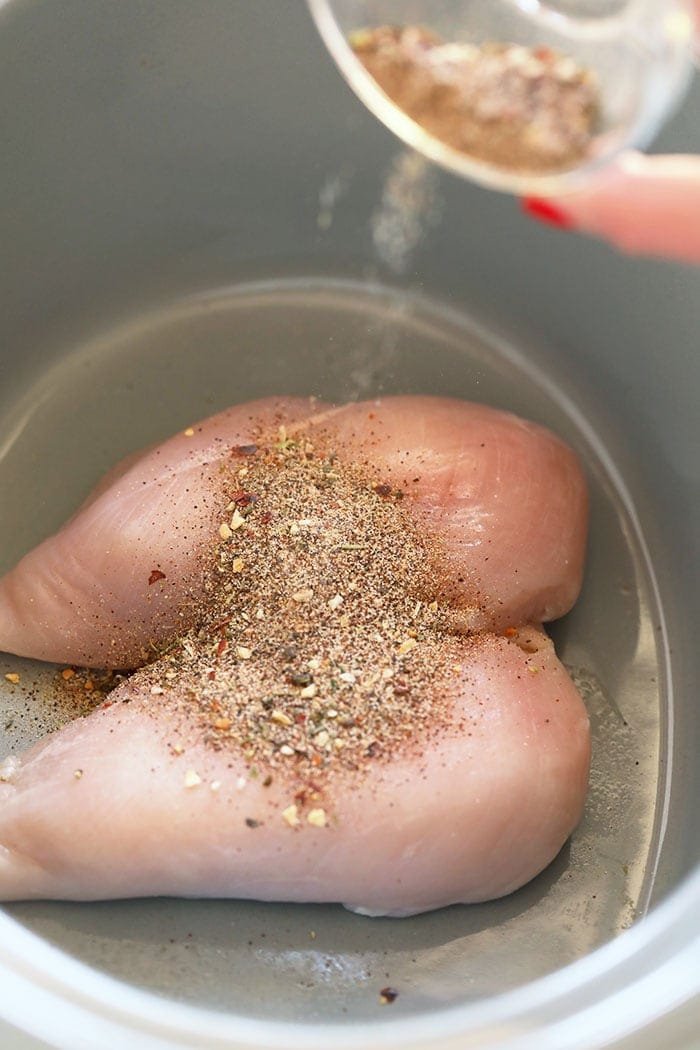 Raw chicken breasts in a pot being seasoned with spice rub
