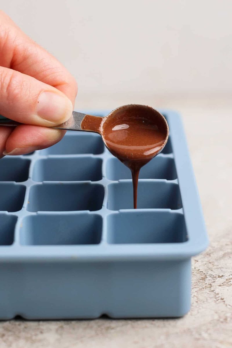 Melted chocolate being spooned over pressed protein bite cubes
