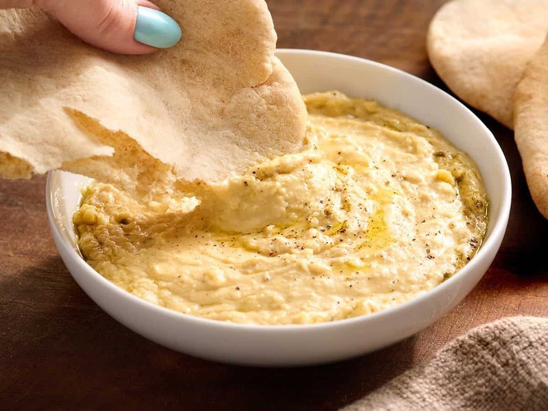 Hand dipping a pita wedge into hummus