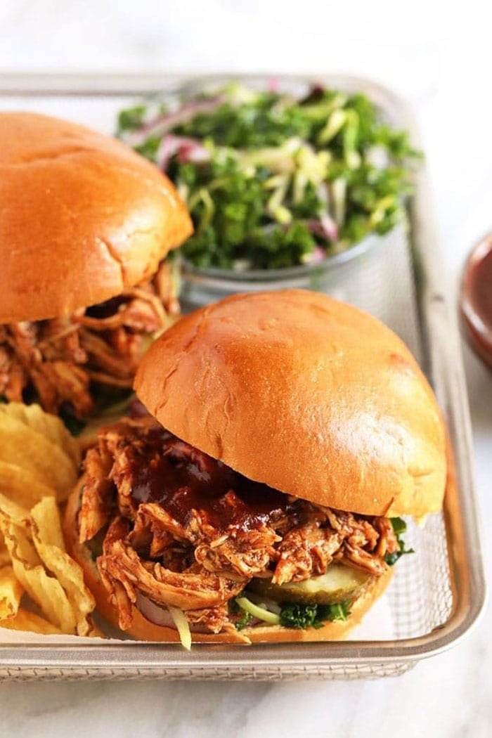Close-up of saucy pulled chicken sandwich with pickles and slaw