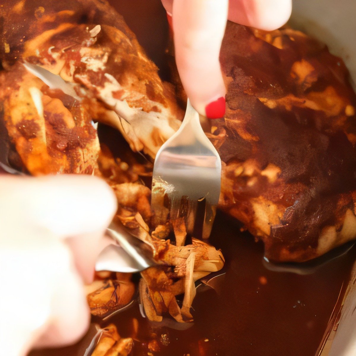 Hands shredding saucy slow-cooked chicken with two forks